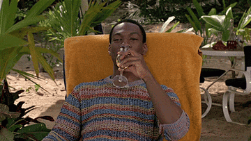 a gif of Eddie Murphy in the movie &quot;Trading Places&quot; laying on a beach with a glass a champagne