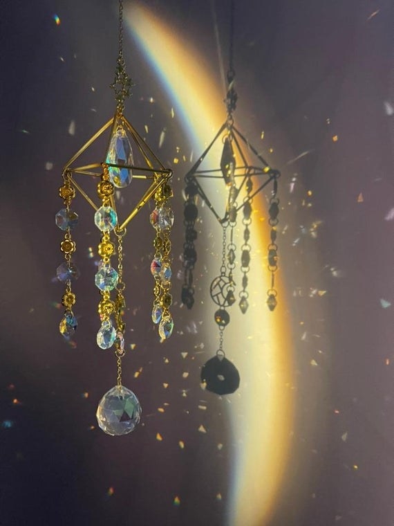 The crystal suncatcher is shown with light beams shining through it, casting many rainbows on the wall behind it