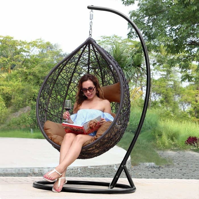 A woman sitting on the swing while having a drink and reading a magazine
