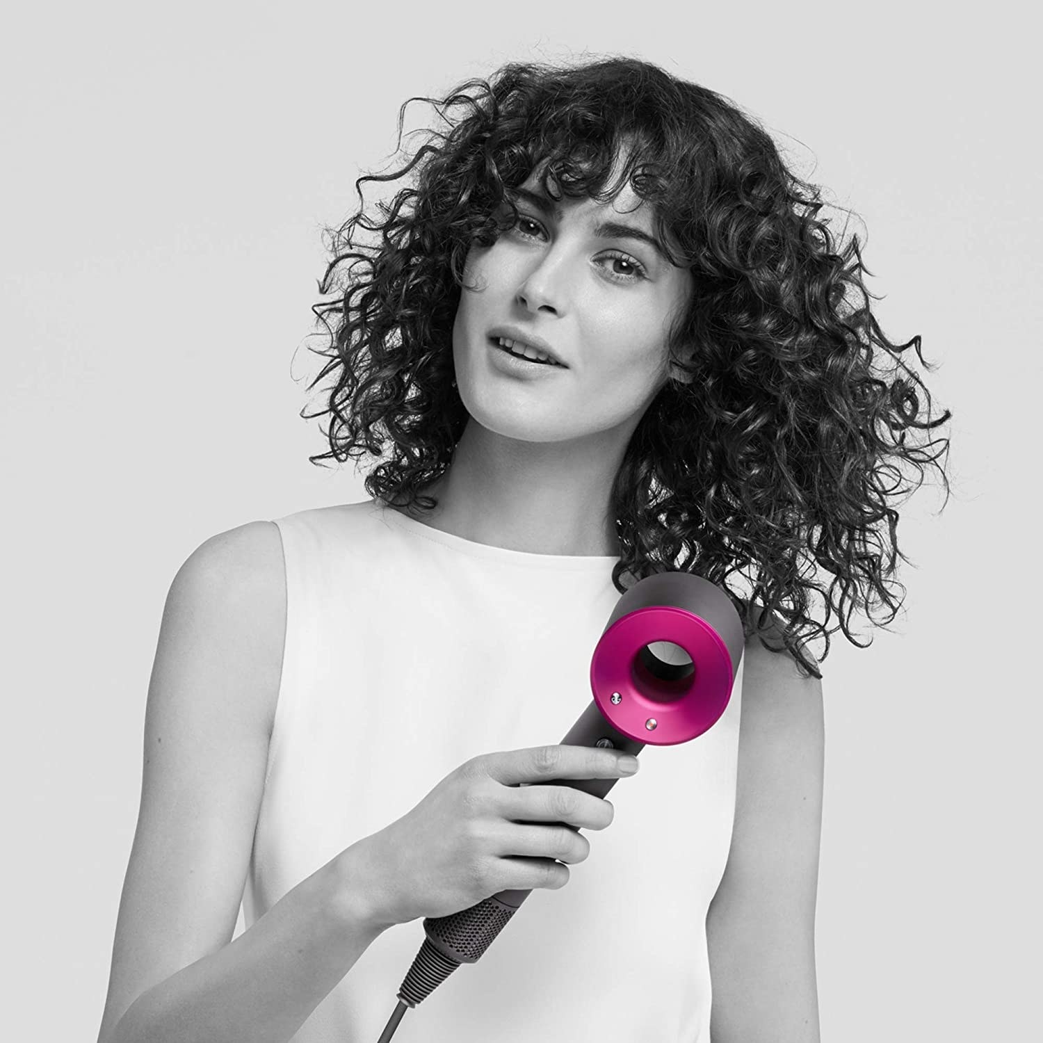 An image of a curly haired woman using dyson hair dryer on her hair