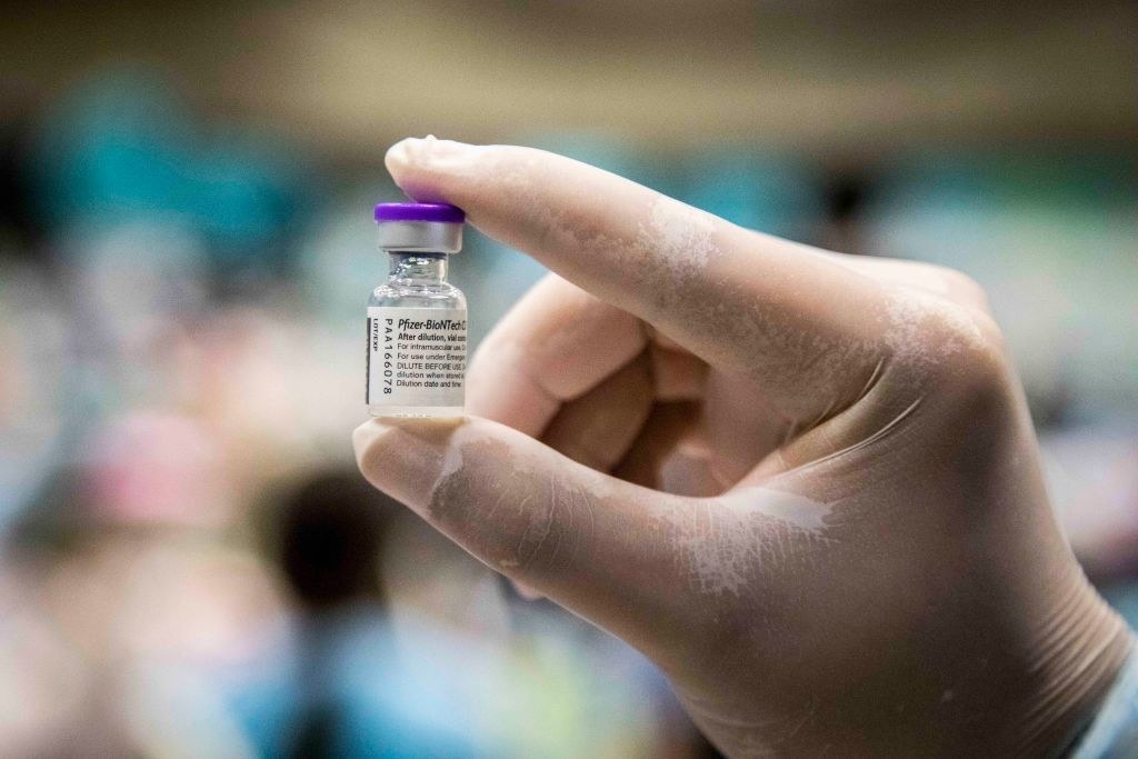A closeup of a gloved hand holding a vial of the Pfizer vaccine
