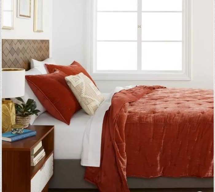 A red velvet quilt on a bed next to a wooden end table