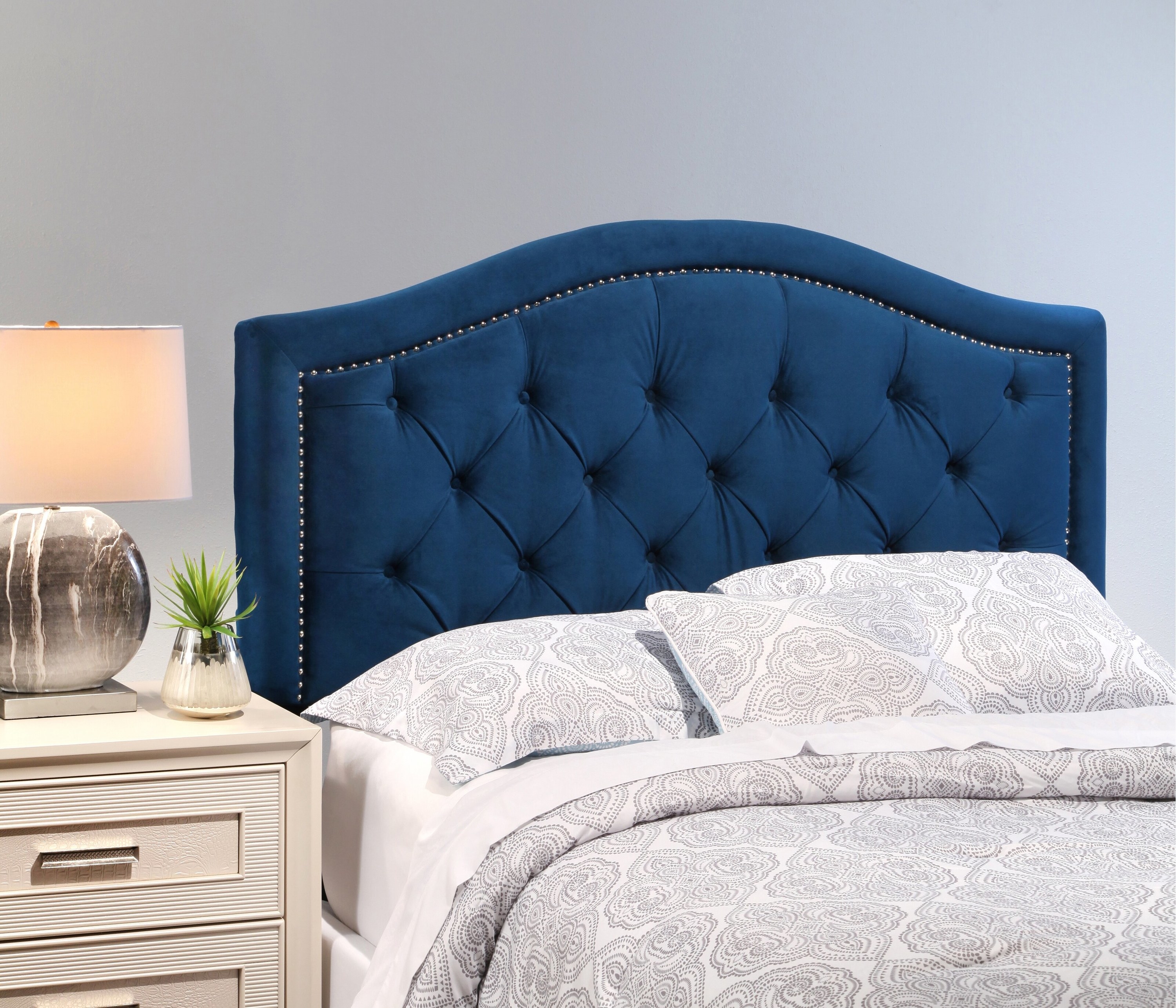 the blue headboard above a bed with gray sheets and a white nightstand on the side