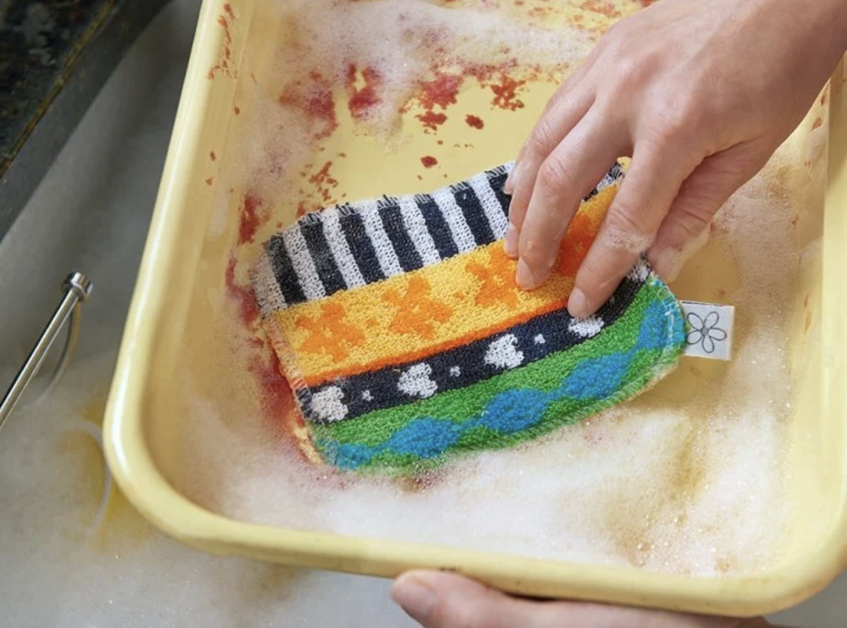 a model&#x27;s hand washing a pot with the scrubbing and scouring pad