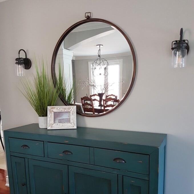 the circle mirror hanging above a blue cabinet with a picture frame and plant on top