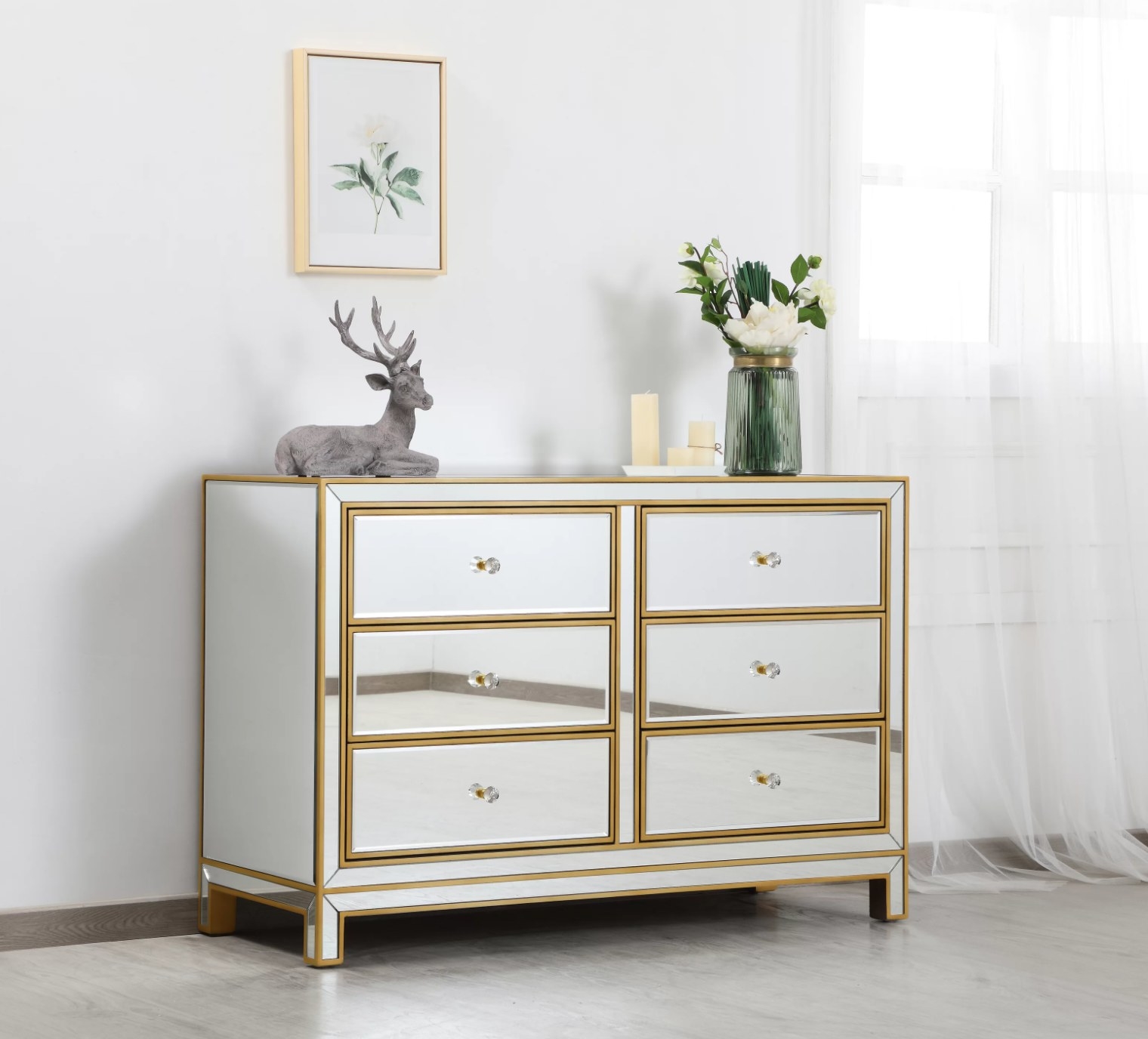 the mirrored dresser with gold accents. there&#x27;s a deer decoration and vase of flowers on top