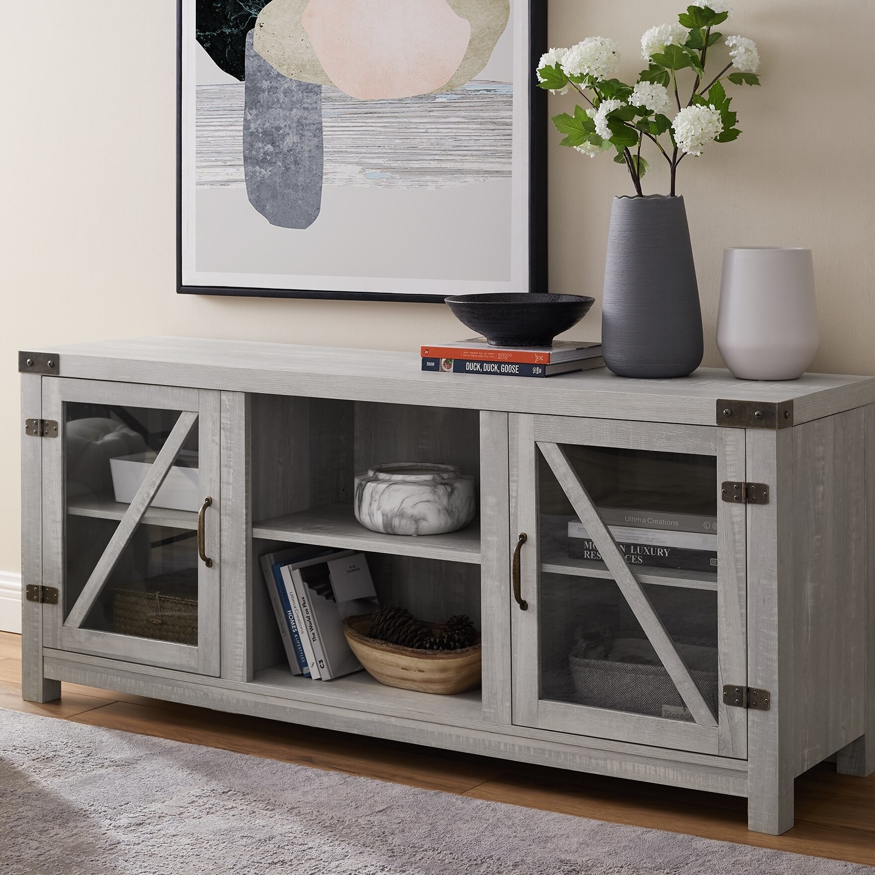 the light gray tv stand with books in each of the cupboards, vases on top, and two decorative bowls in the open center