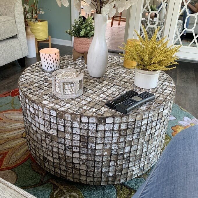 the brown coffee table with coasters, plants, remotes, and a candle on top