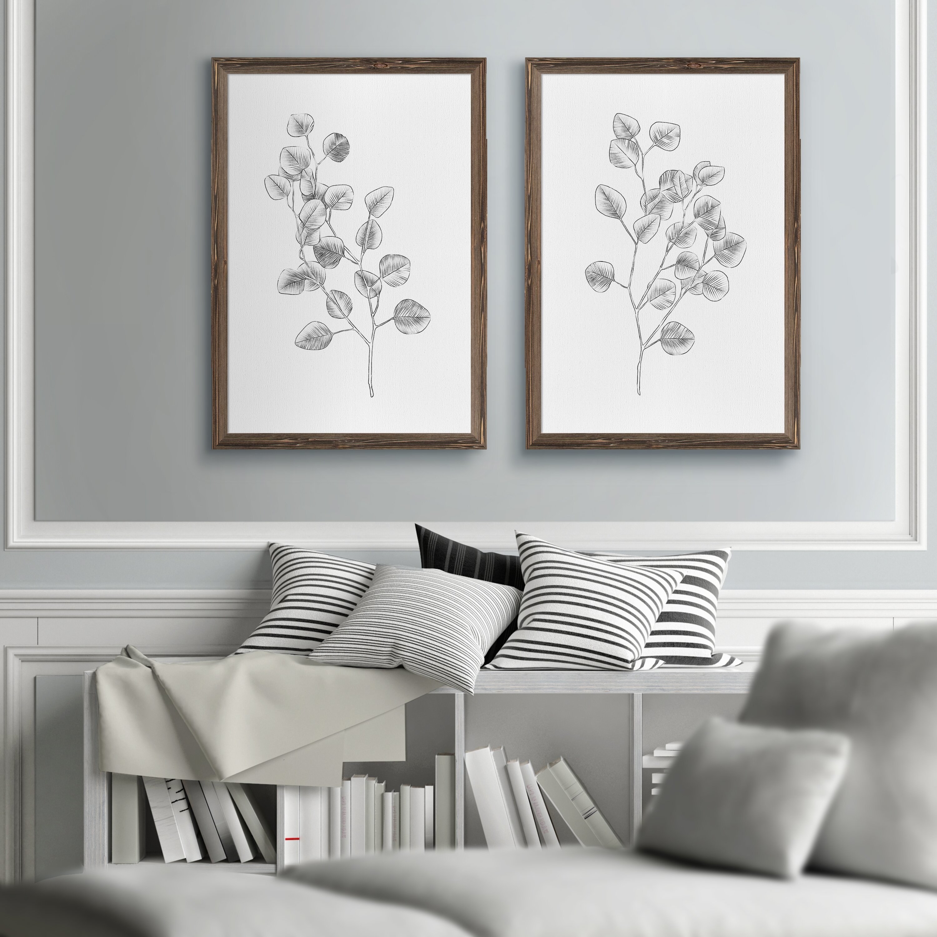 the two framed eucalyptus plant sketches hanging on a wall above a couch and pile of pillows