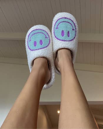 a model wearing the slippers with a blue and purple smiley face