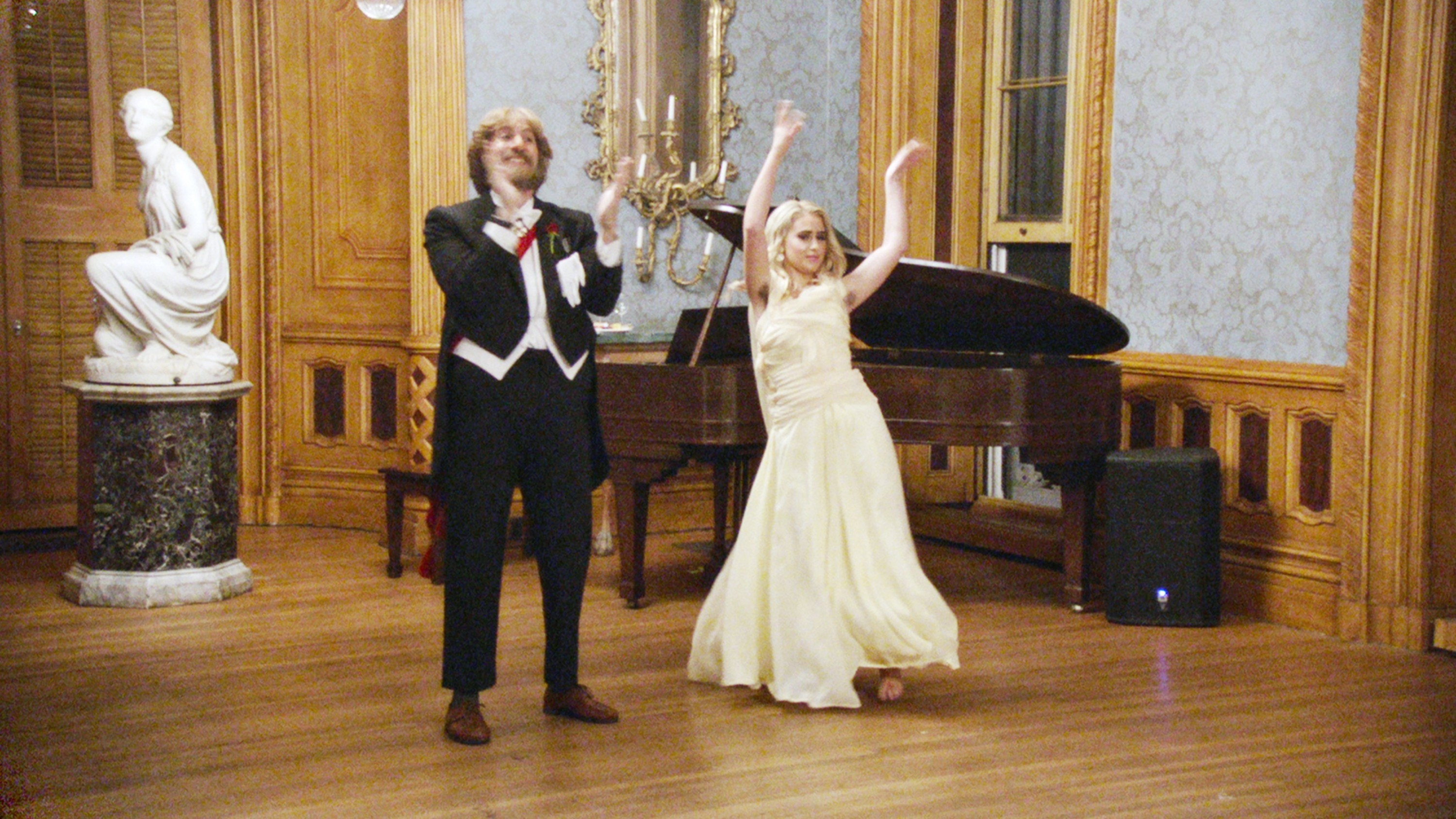 Sacha Baron Cohen and Maria Bakalova dance together in formalwear in a ballroom