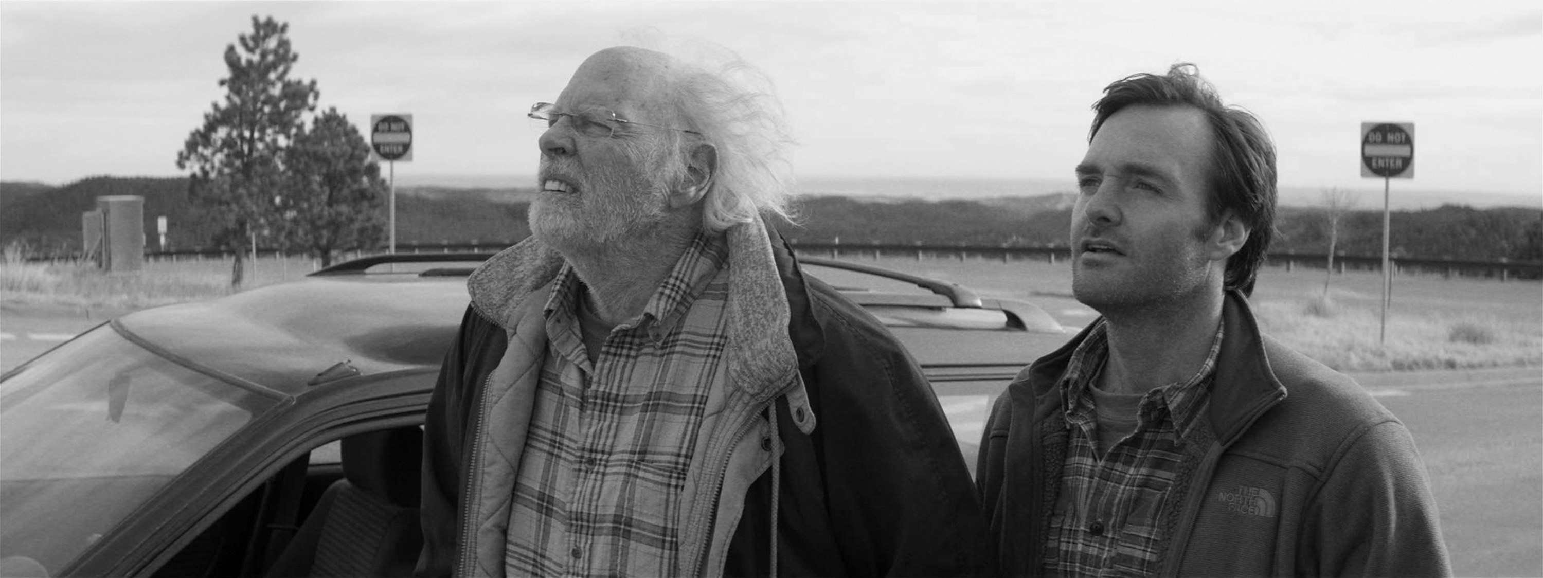 Bruce Dern and Will Forte stand in a parking lot in black and white