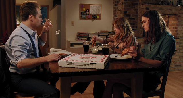 Sam Rockwell, Chloe Grace Moretz, and Kiera Knightley eat pizza at a dining room table