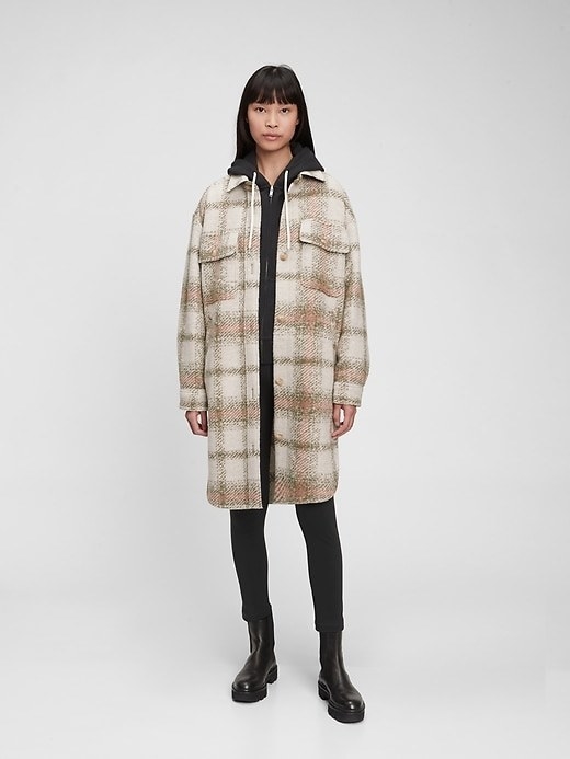 Model is wearing a beige plaid jacket with a black top and black pants