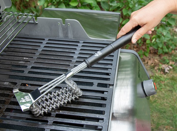 a model using the grill brush to clean an outdoor grill grate