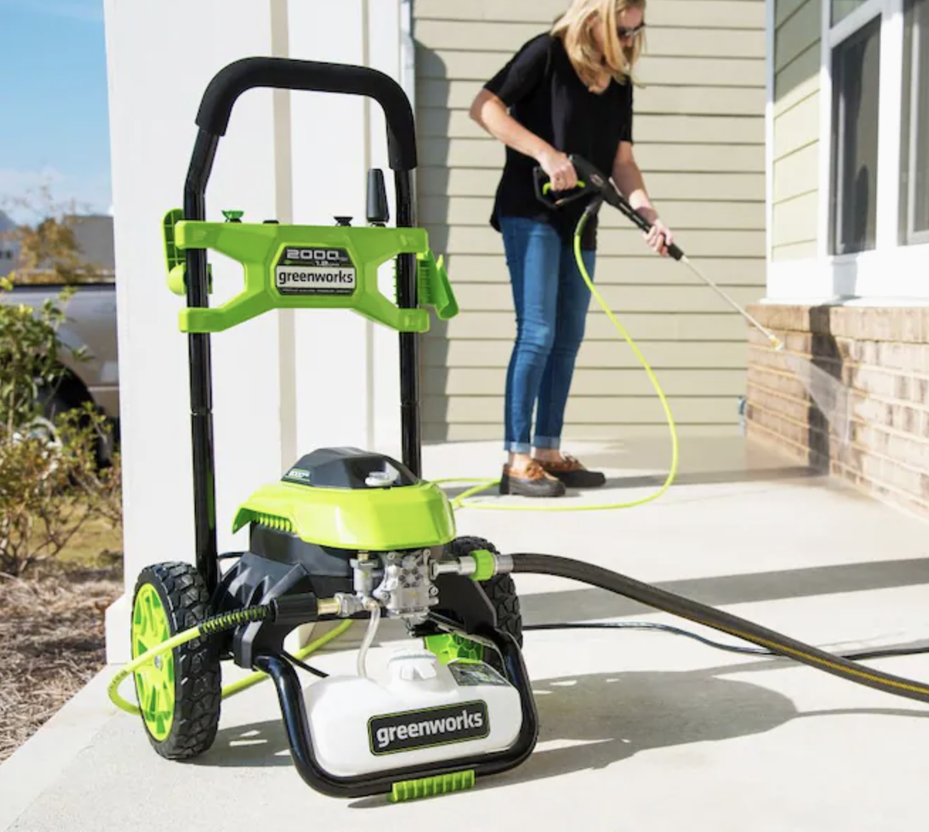 Model using the green accented vacuum-shaped pressure washer&#x27;s hose to clean the side of a home