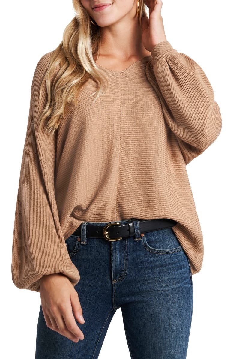 Model is wearing a tan balloon sleeve sweater and denim jeans