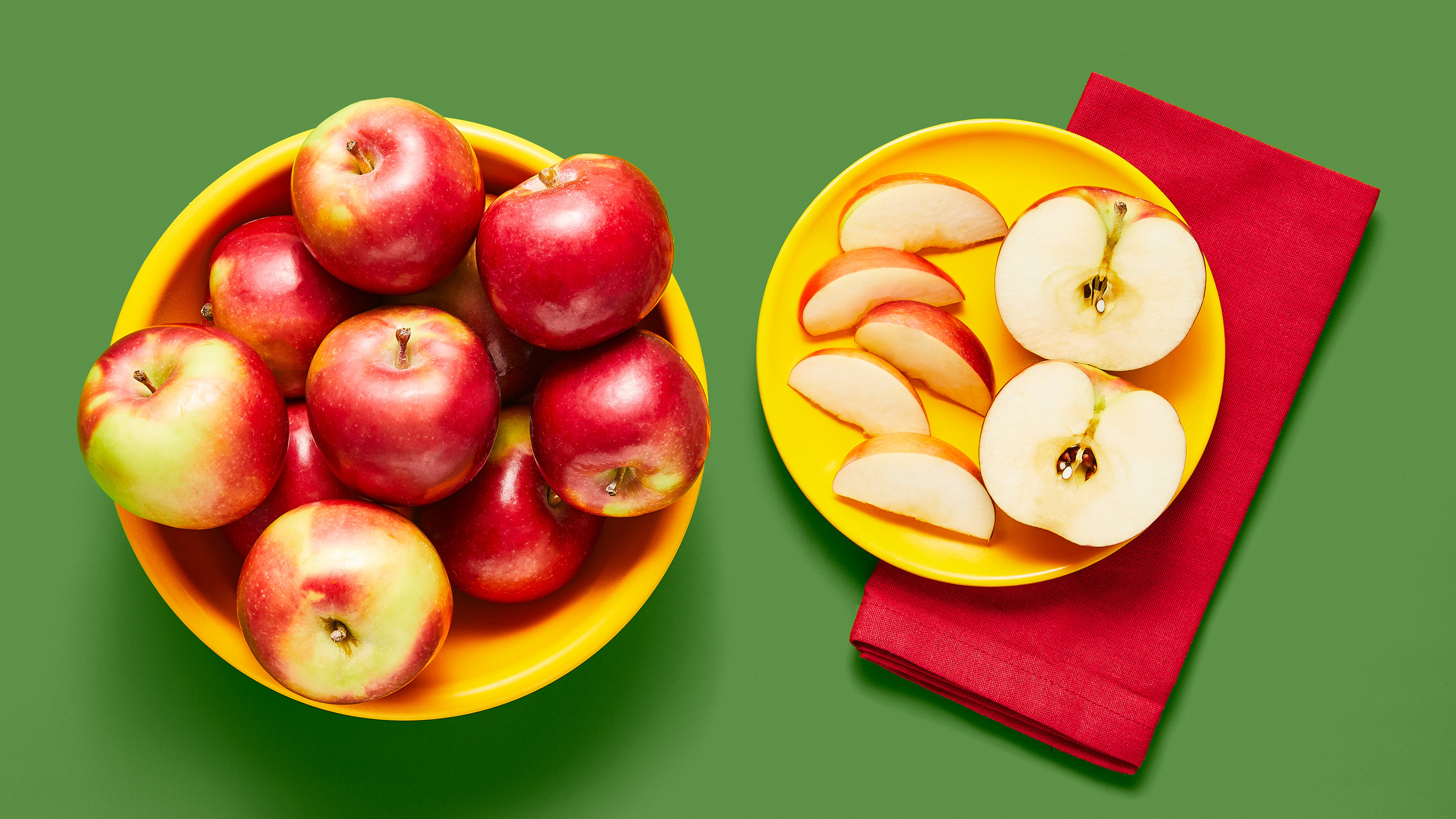 A plate of sliced apples sits beside a larger bowl of whole apples