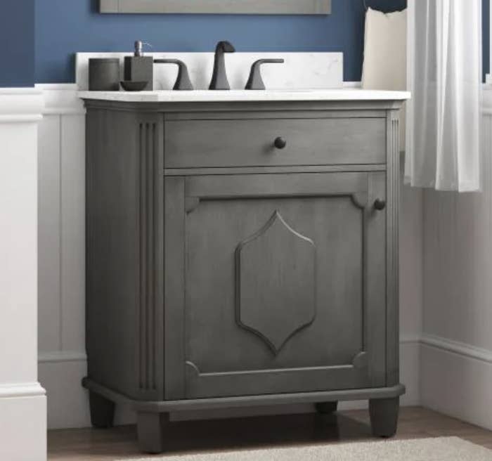 a dark gray single sink vanity with a white top, a top drawer, and a cabinet