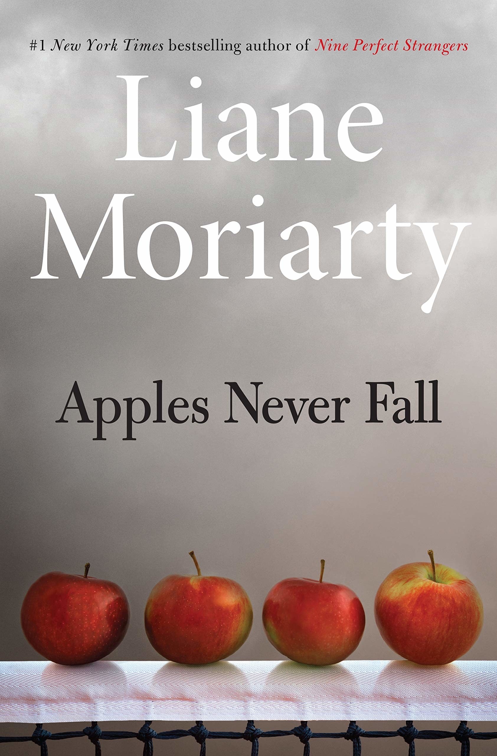 Book cover for &quot;Apples Never Fall&quot; by Liane Moriarty, featuring four apples on top of paper towel-covered barbed wire