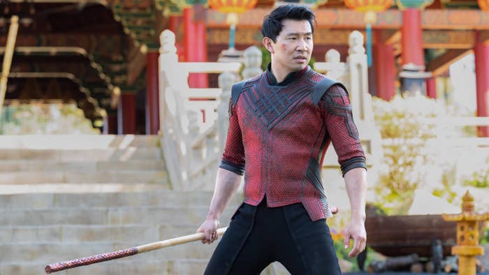 Simu Liu as Shang Chi; he is gripping a long wooden stick and is in battle