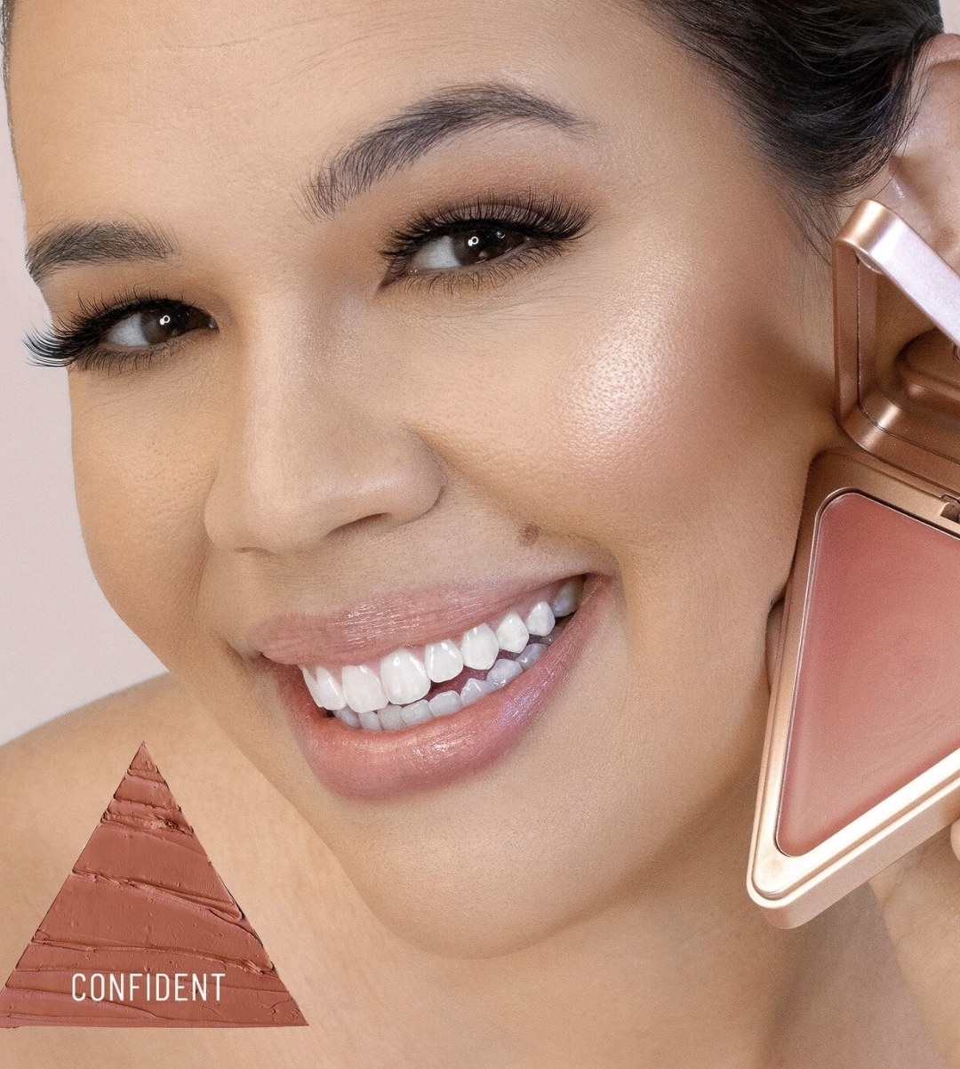 An adult is smiling while holding up the triangular shaped blush up to their cheek, and there is a triangular texture shot that says "CONFIDENT" in the bottom left corner