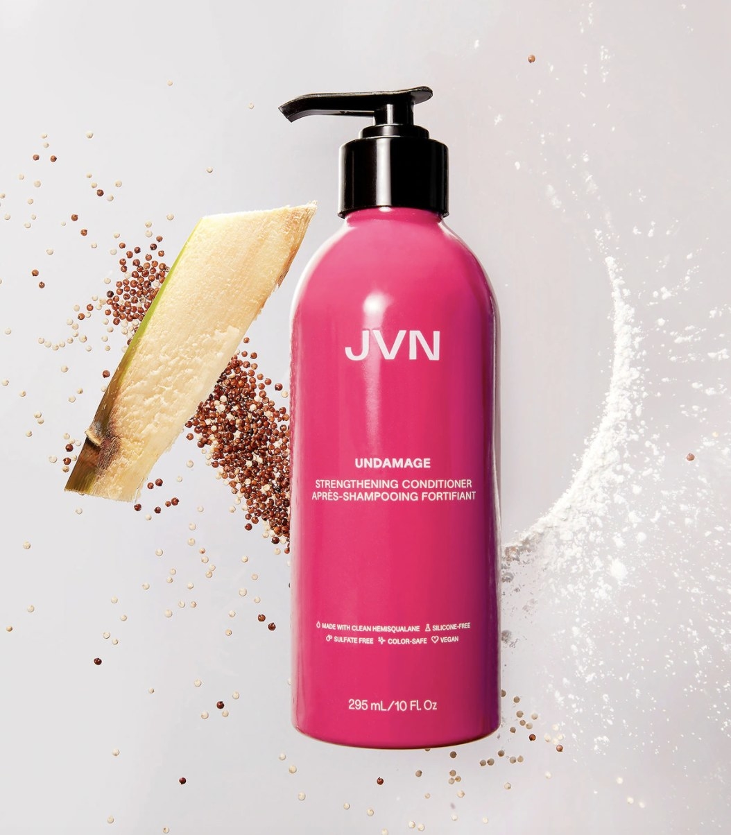 The pink bottle with a black pump spout says "JVN UNDAMAGE" and has has some of the items in the formula rested against the background behind the bottle