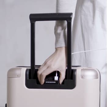 A model charging their phone in the hidden compartment in the suitcase handle 
