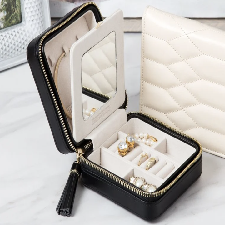 The black zippered case open to show white interior lining holding rings, earrings, and necklaces