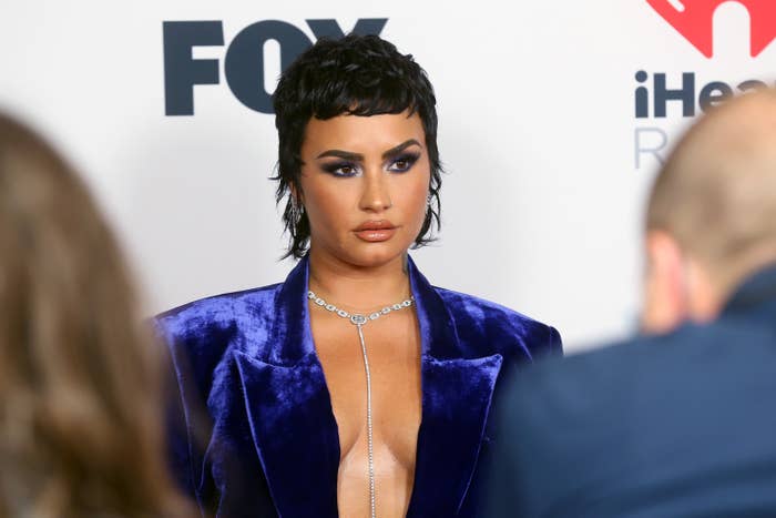 Demi wearing an open velvet blazer and diamond necklace posing for photographers on the red carpet