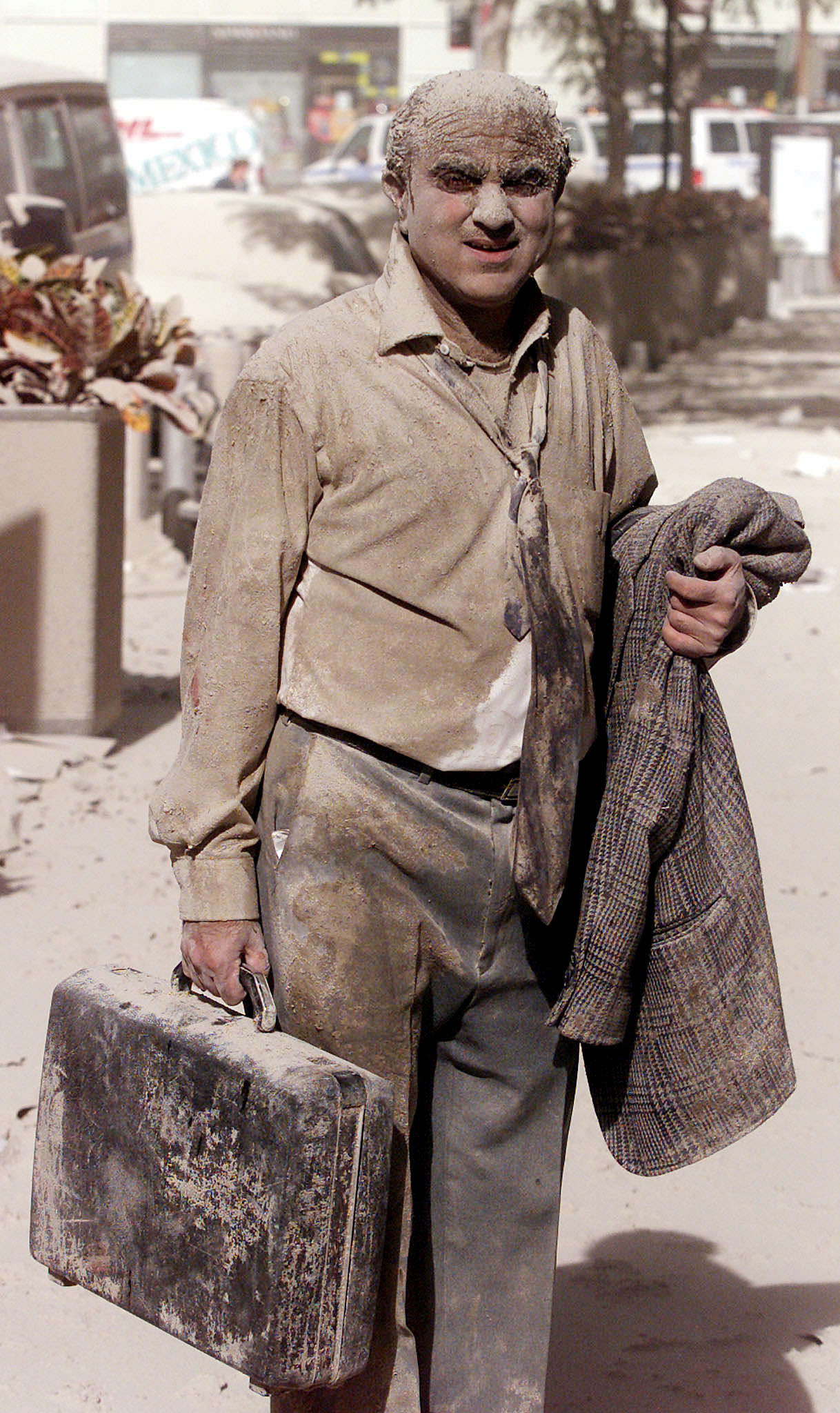 A man holding a briefcase and suitcoat totally covered in dust and ash