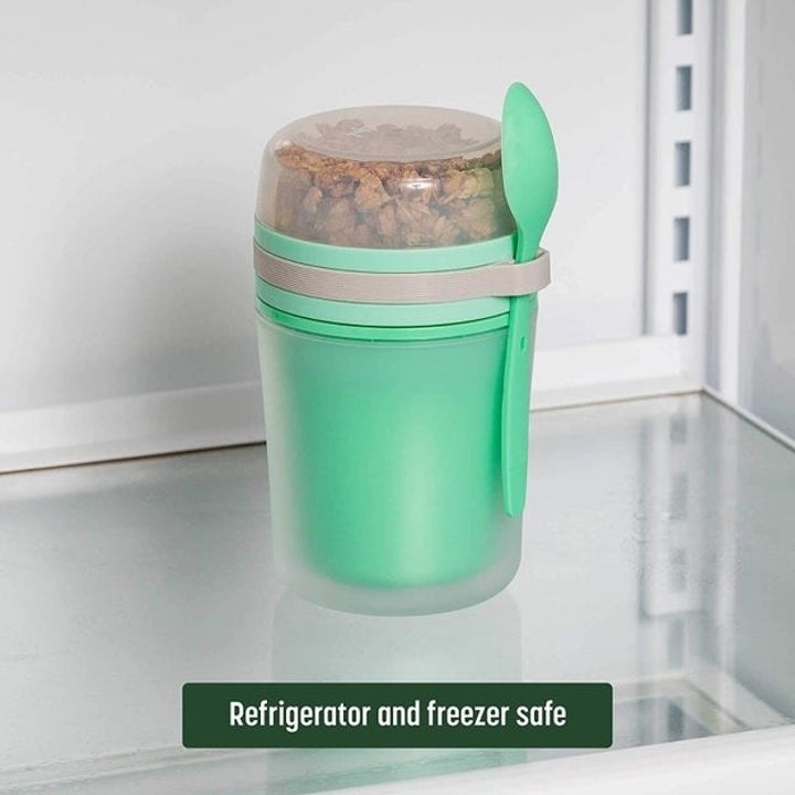 The container closed and packed together with the spoon in the holder in a fridge. Text reads "Refrigerator and freezer safe"