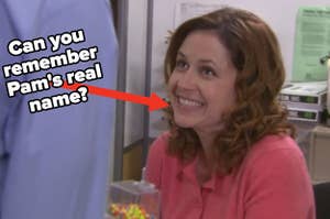 Pam Beesly smiles up at someone off screen while sitting at her desk in "The Office"