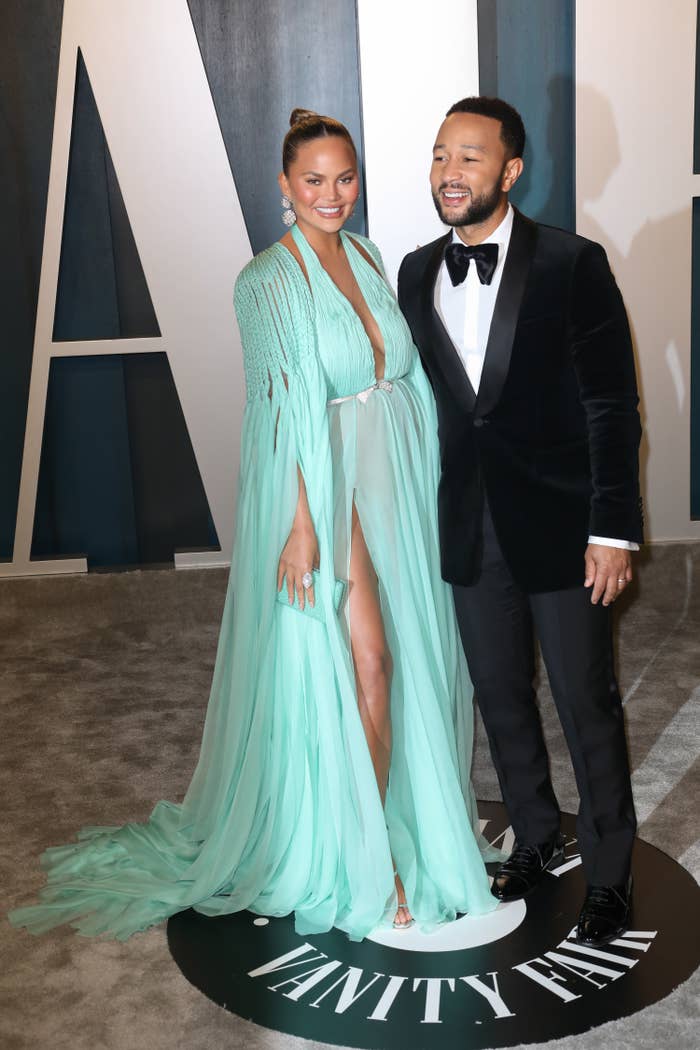 Chrissy, in a long flow-y gown, poses with her husband John Legend at an Oscars after party