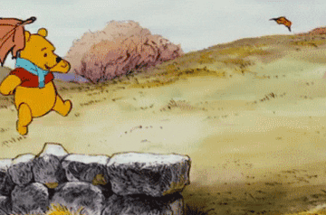 a gif of pooh skipping on a stone wall with leaves floating by