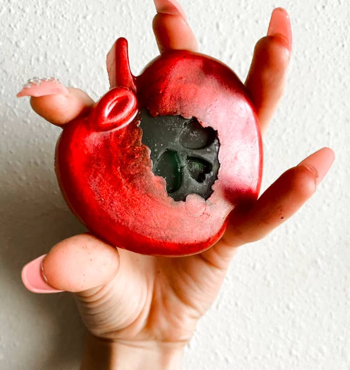 hand holding an apple-shaped soap bar with a skull's face emerging from the middle of the apple. when I said wicked good, oh I meant wicked good.