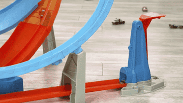 GIF of toy cars speeding around a large looped Hot Wheels track