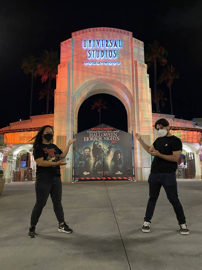 Crystal and Pablo standing outside the entrance to Horror Nights, pointing at the sign