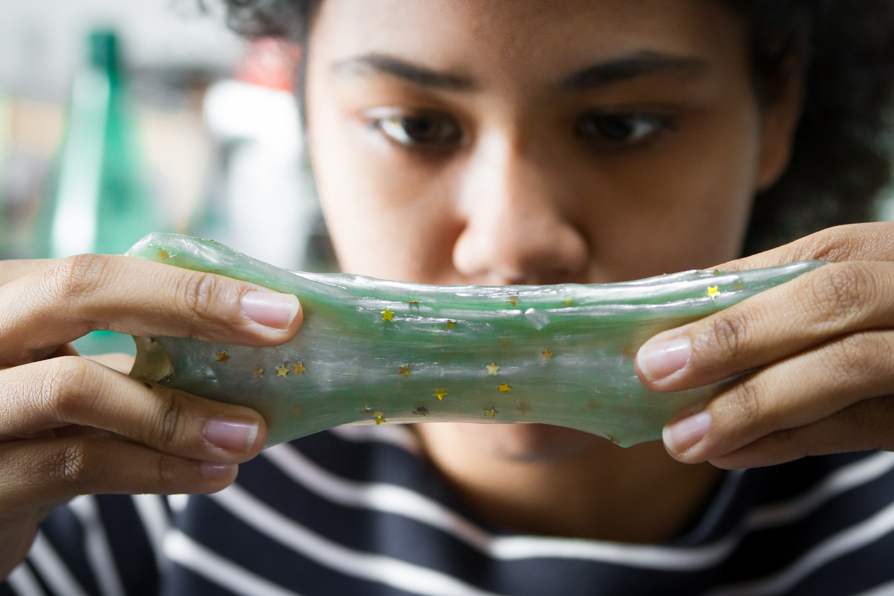 A girl looks intently at a glittery and stretched piece of slime she is stretching between her hands.