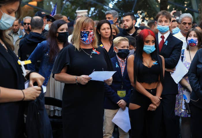 Somber people, most wearing masks, stand together