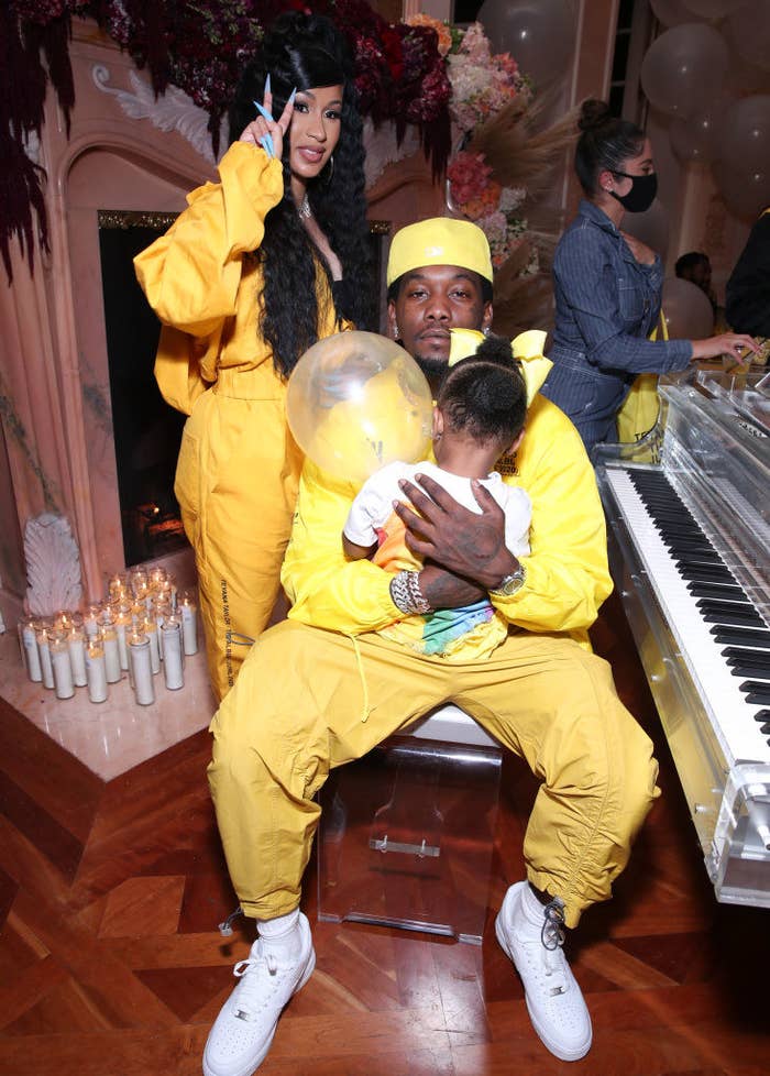 Cardi standing next to Offset is sitting at a piano while holding their daughter Kulture