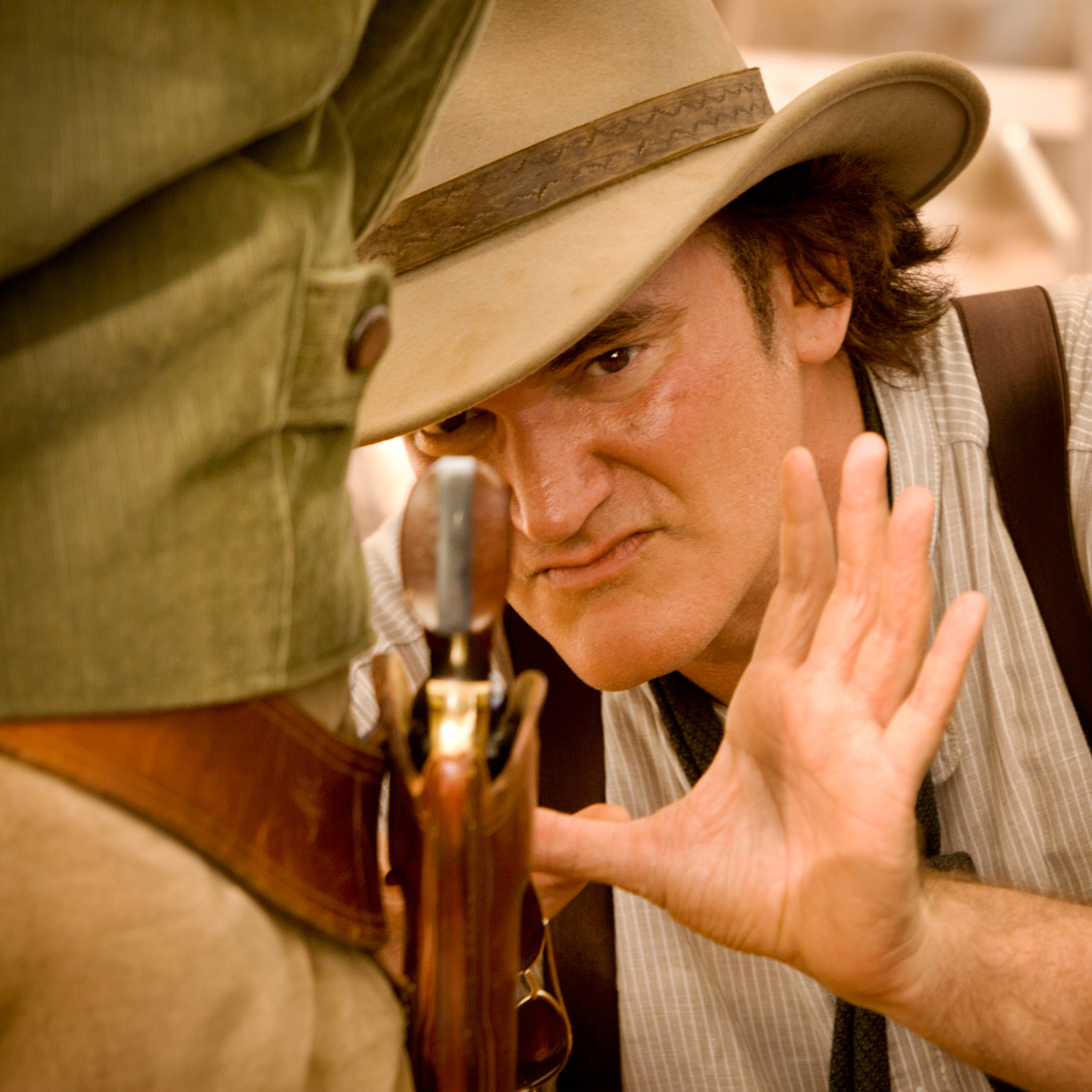 A close up of Quentin Tarantino as he leans in closely to examine a gun on someone&#x27;s belt