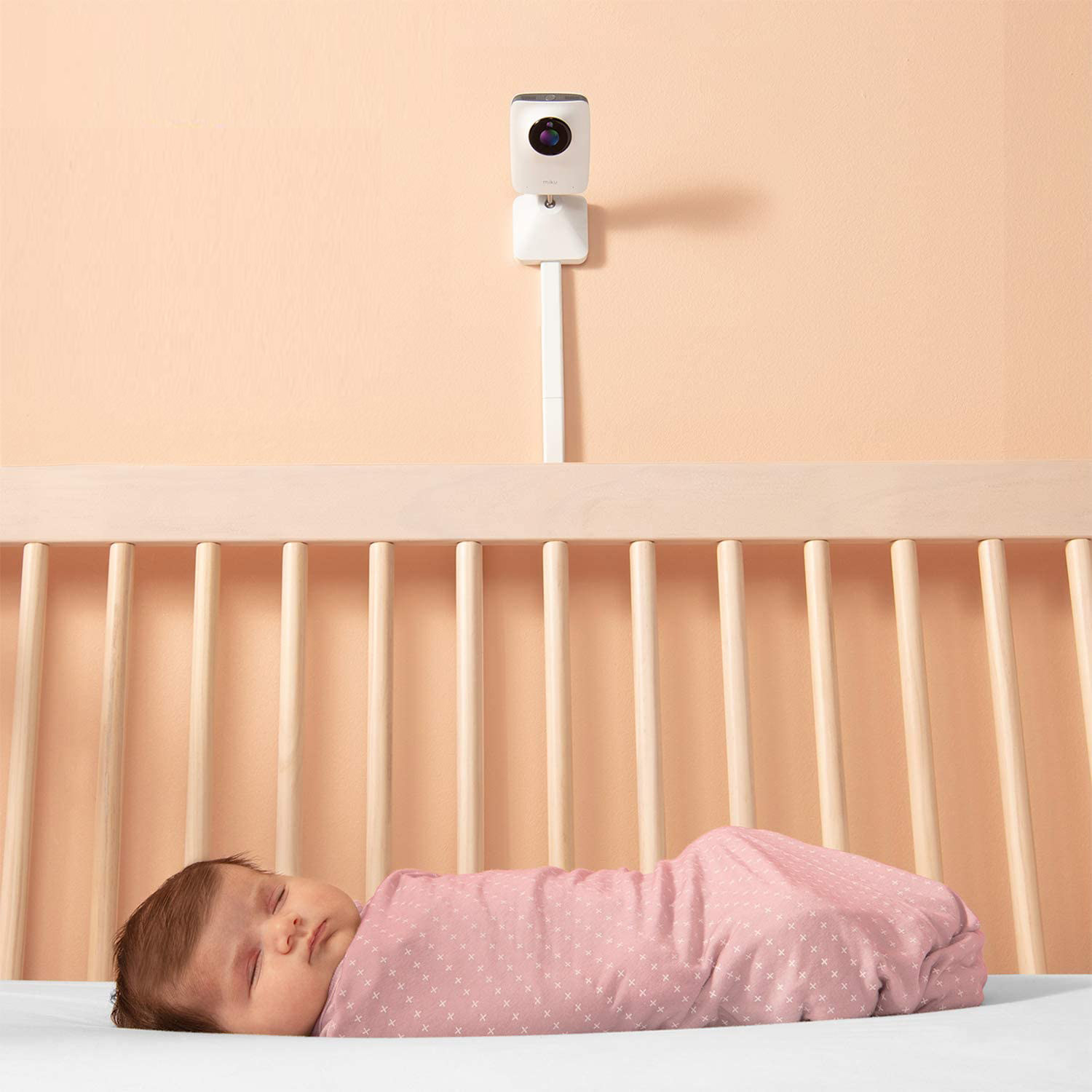 A baby sleeping in a crib with a camera on the wall beside the crib