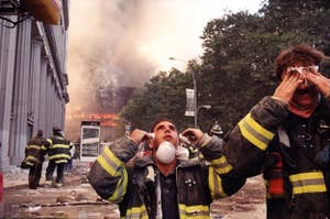 Firefighters wipe their eyes as buidlings burn in the background