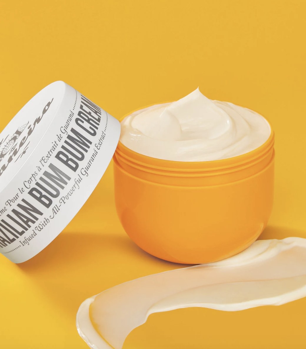 The orange container is holding white cream and has a white lid that says &quot;BRAZILIAN BUM BUM CREAN&quot; against an orange background