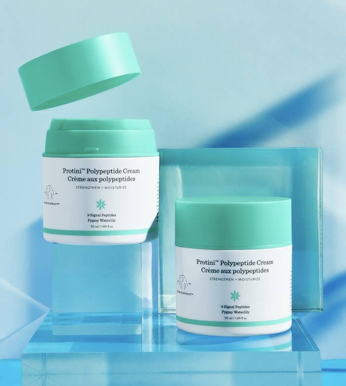 There are two bottles of the teal and white package product against a blue background with clear blocks