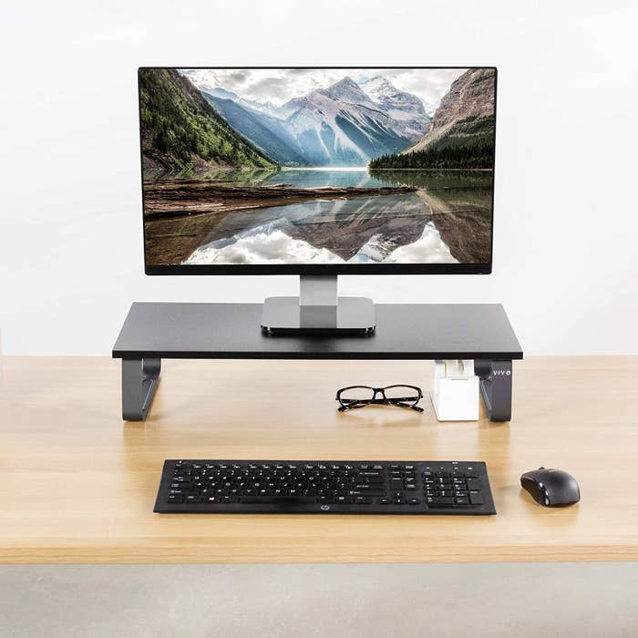 A laptop that is on a high metal stand with a keyboard and mouse on the desk