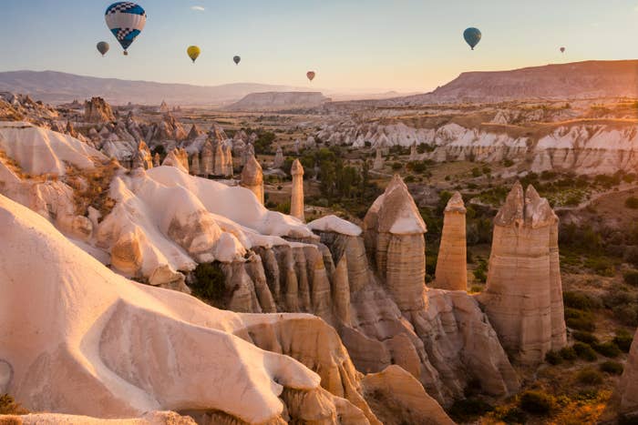 Goreme fairy chimneys. Tall pillared rock formations with hot air balloons floating overhead.