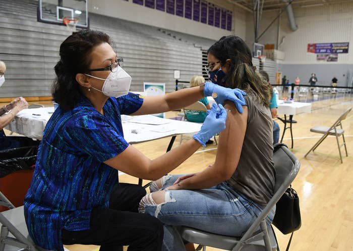 A woman wearing a mask administers a vaccine to a patient