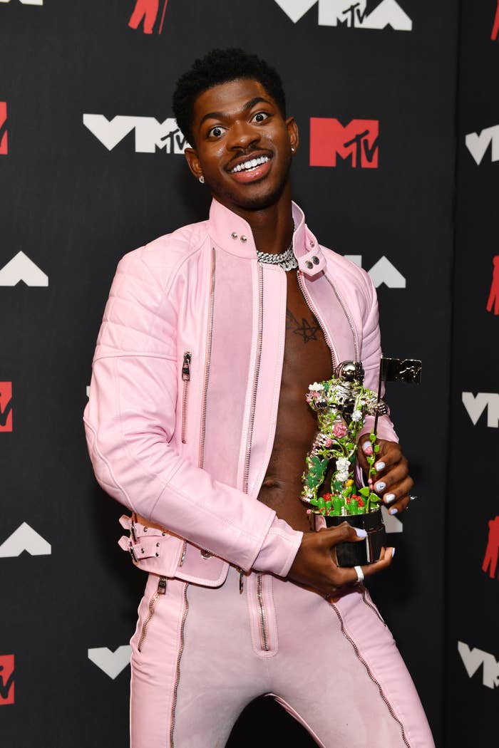 Lil Nas X posing with his award in a matching leather jacket and pants set